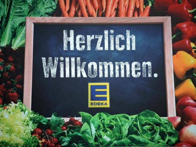Herzlich Willkommen. Text auf einer Tafel, rundherum frisches Gemüse